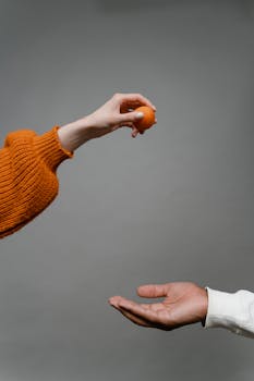 Close-up of two hands passing a small orange ball, symbolizing cooperation.